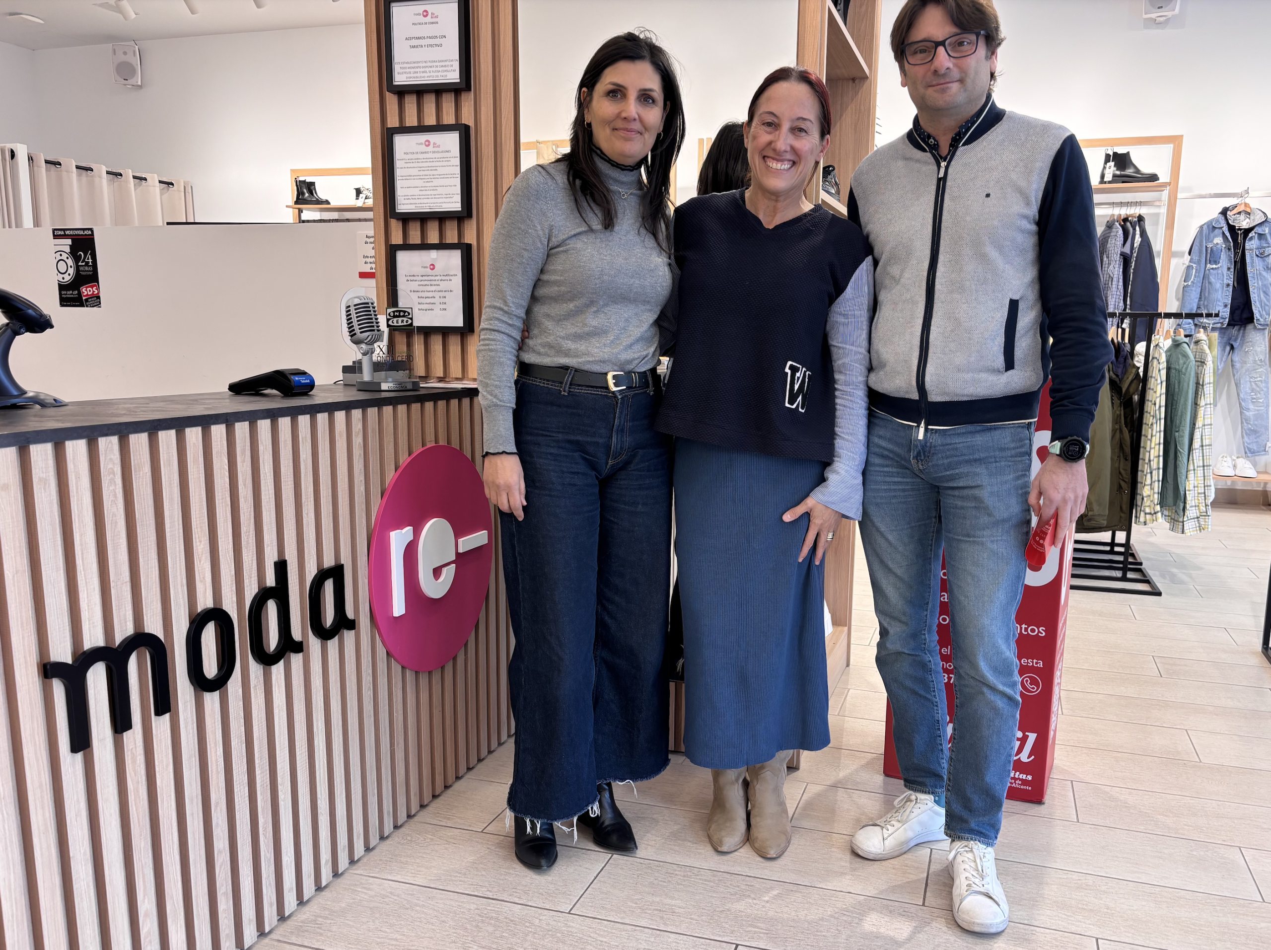 Helena, Inma Lara y Jesús Martínez posan en el interior de una tienda Moda re-, junto al mostrador, durante la visita del Clúster de Economía Circular al proyecto Retextil.